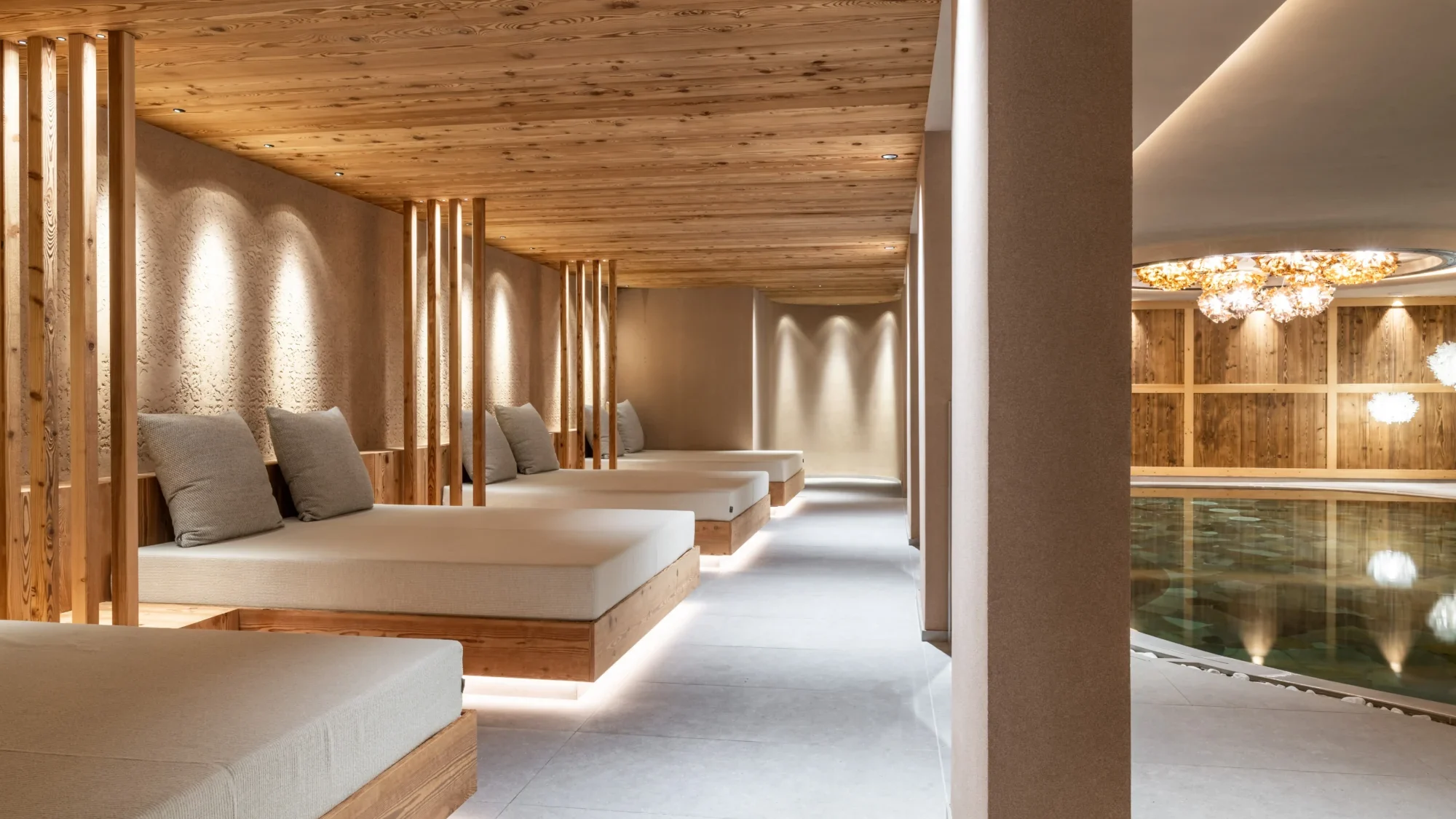 Ein stilvoller Wellnessbereich mit Liegen aus Holz neben einem Innenpool.