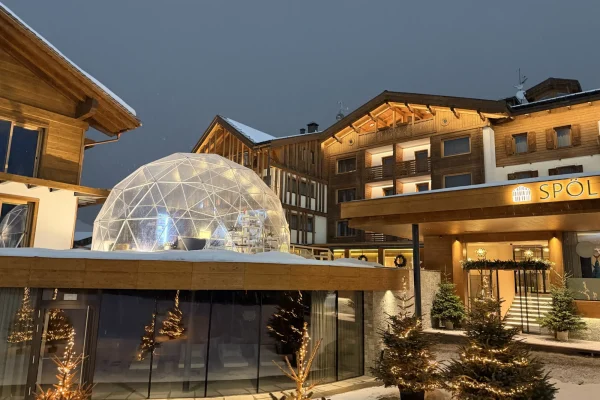 Snowy evening scene of a cozy hotel with a glowing geodesic dome.