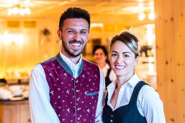 Due camerieri sorridenti in un ambiente luminoso di ristorante.